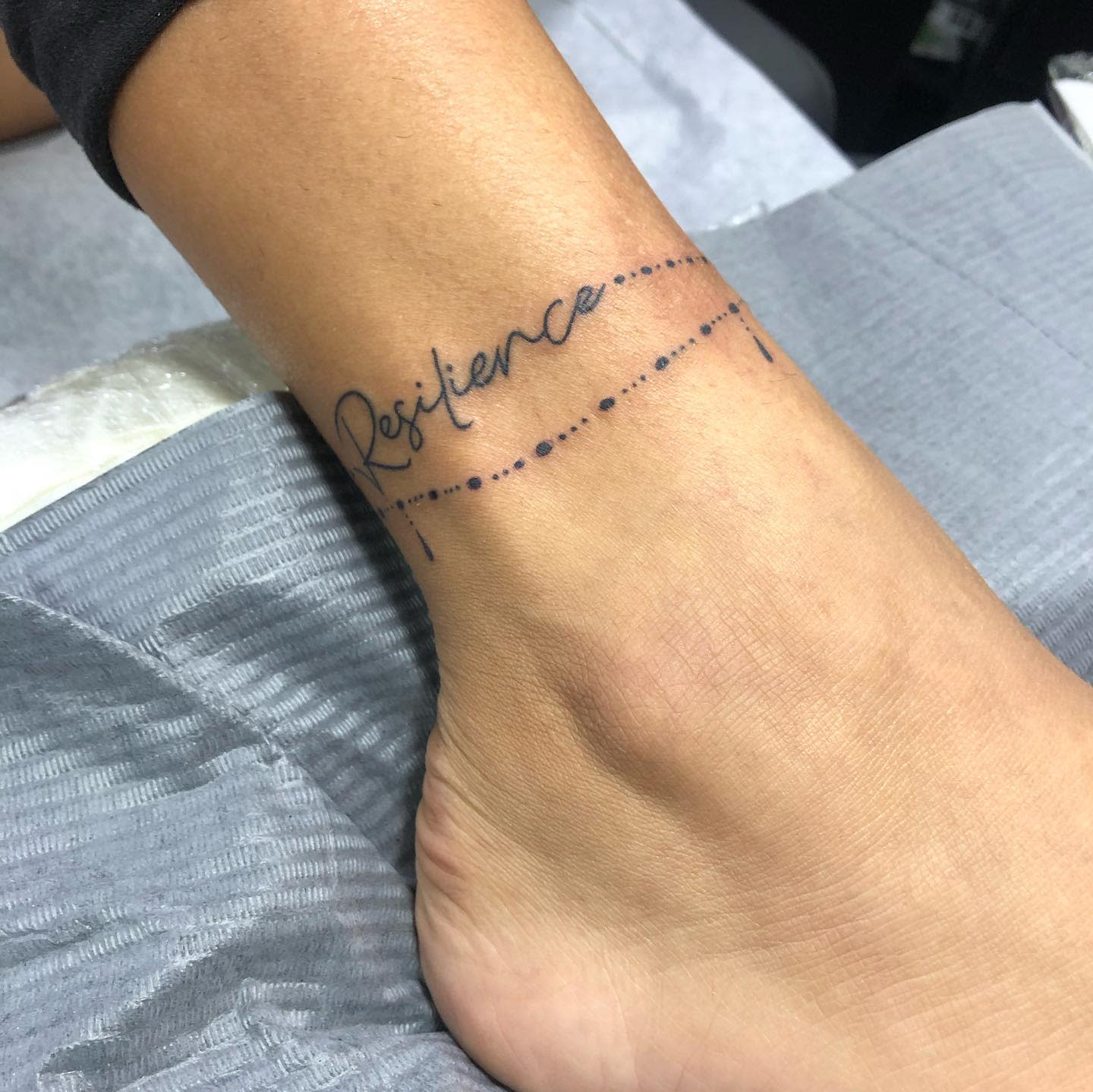 Tattoo on ankle with the word "Resilience" and a dotted line design