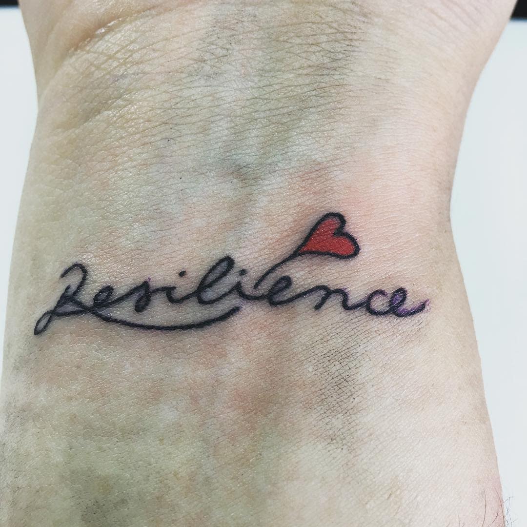 Tattoo of the word "resilience" with a small red heart on a wrist