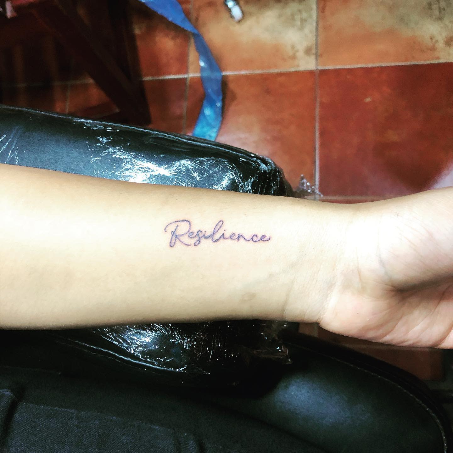 Forearm tattoo with "Resilience" written in cursive script