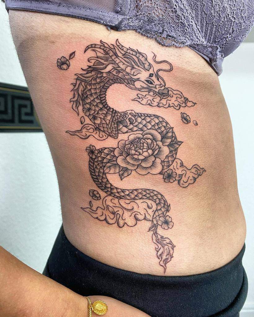 Tattoo of a dragon intertwined with flowers on a person's side