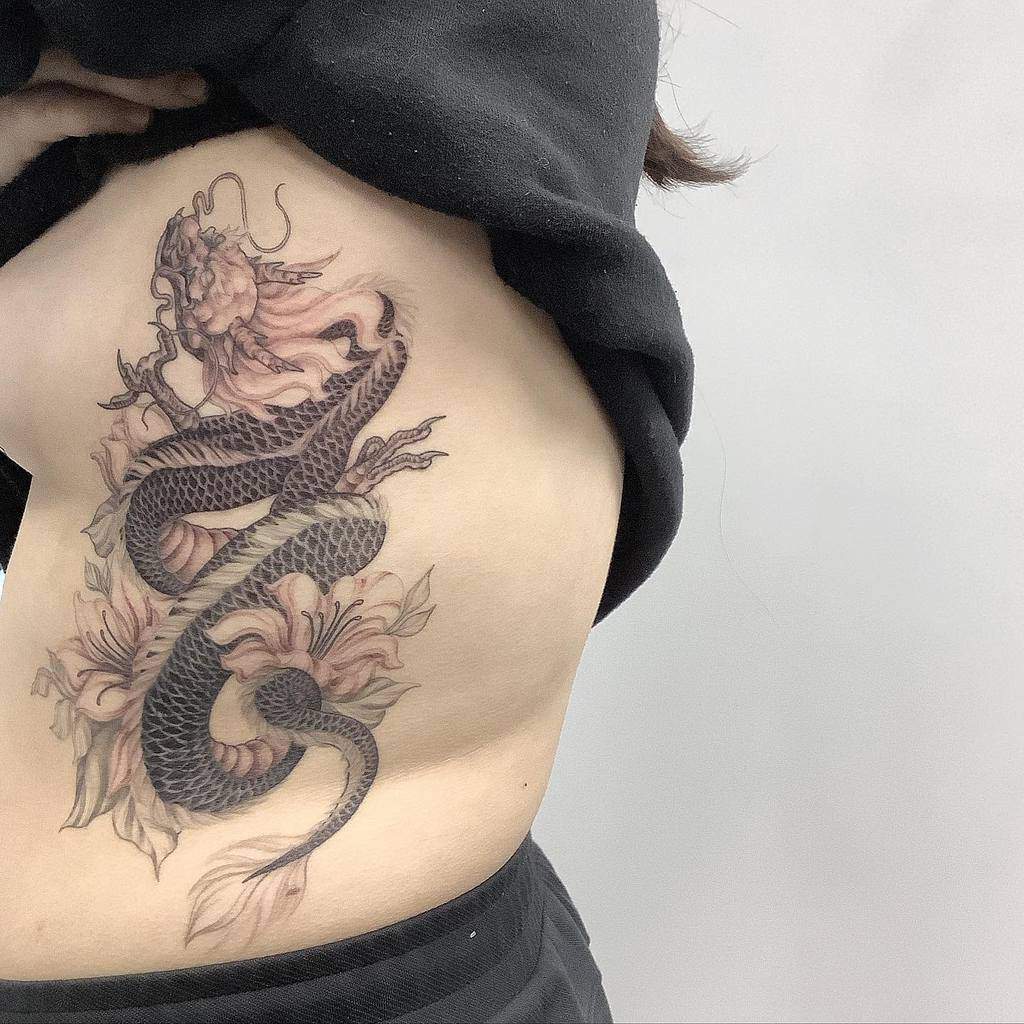 Tattoo of a dragon and flowers on a woman's side and ribcage