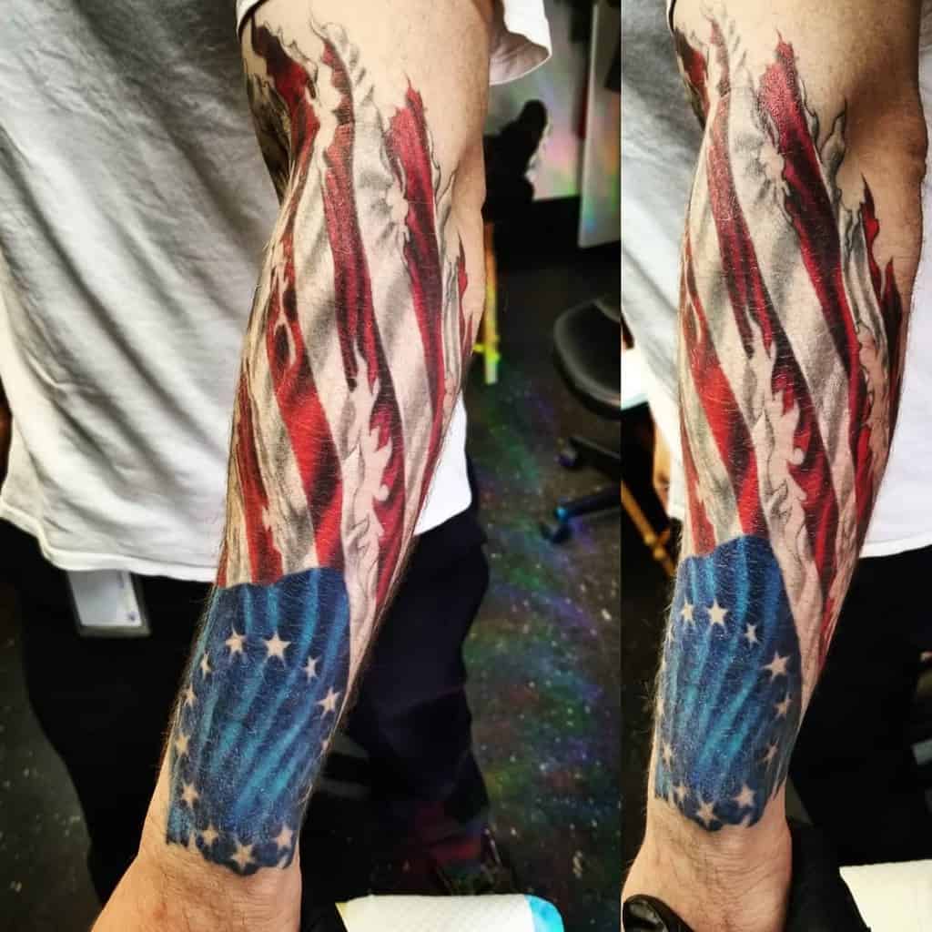 Forearm tattoo of a tattered American flag with distinct red, white, and blue sections