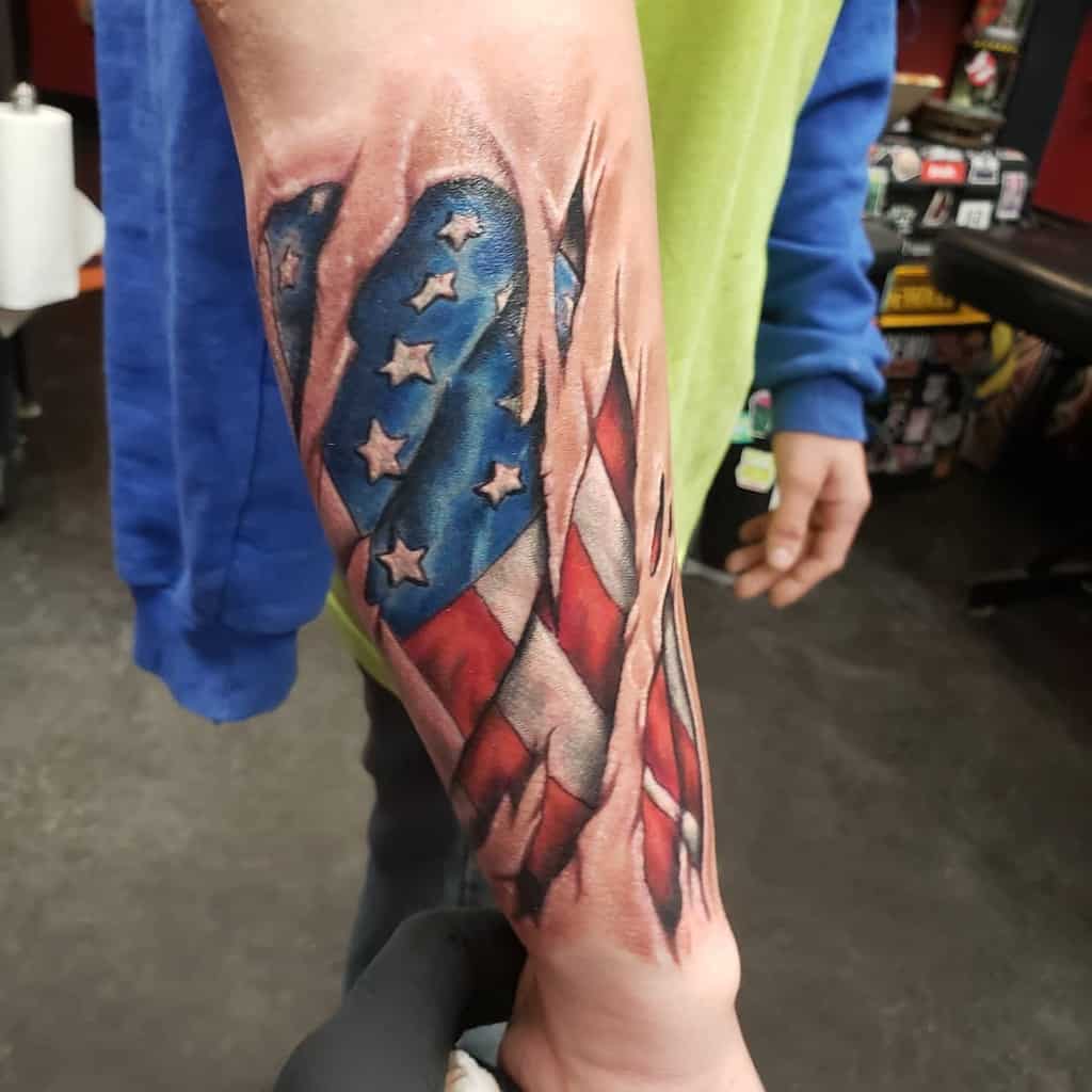 Forearm tattoo of a torn American flag with realistic detailing and colors