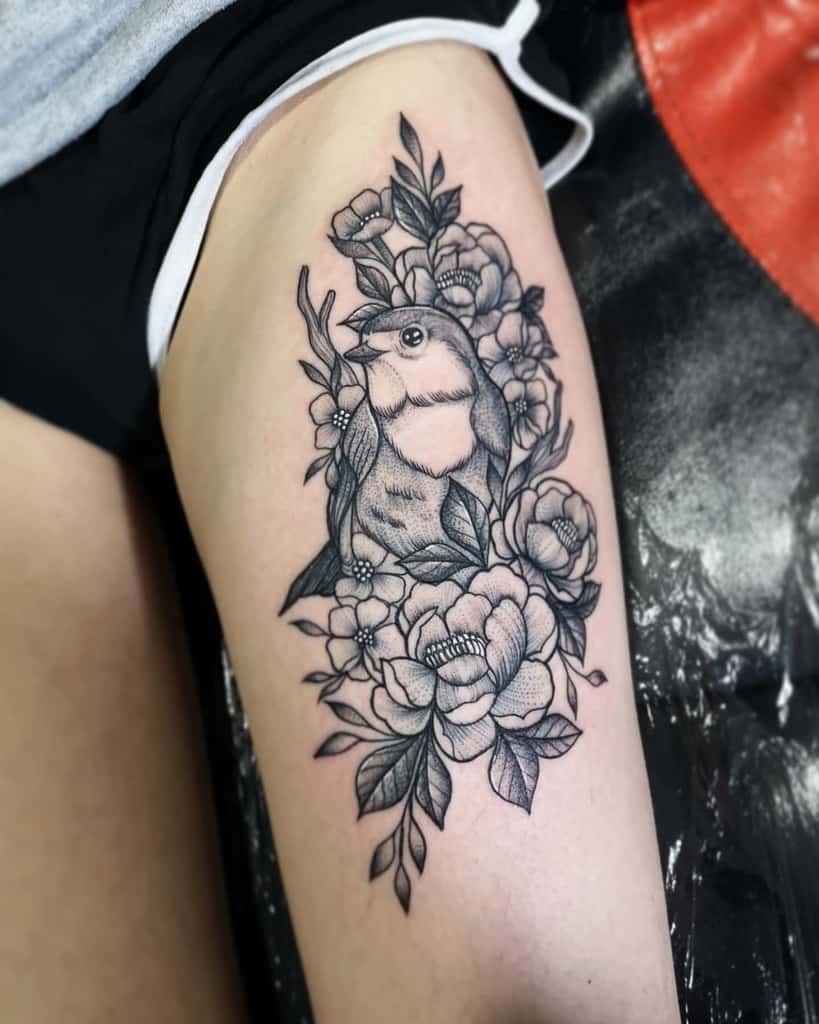 Black and grey tattoo of a robin surrounded by detailed blooming flowers and leaves, featuring intricate shading and fine linework