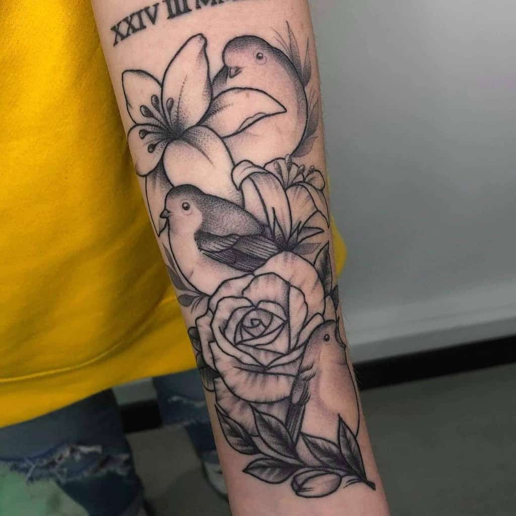 Black and grey tattoo of three robins surrounded by detailed roses, lilies, and leaves, with fine linework and shading