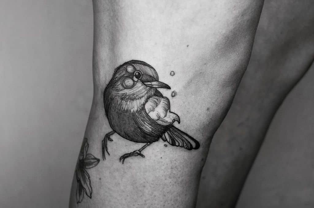 Black and grey tattoo of a robin with fine line shading, standing still with a calm expression, surrounded by small decorative dots
