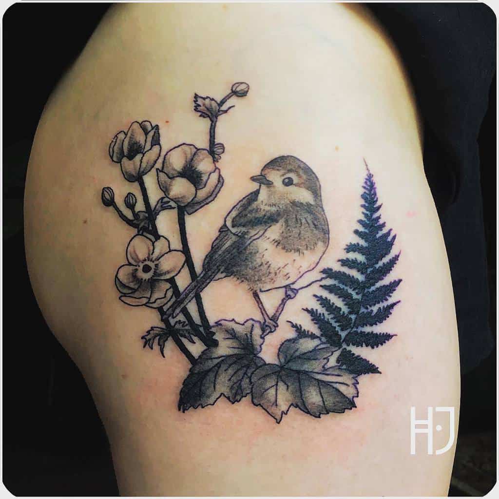 Black and grey tattoo of a robin perched on a branch, surrounded by delicate flowers, leaves, and a fern, featuring fine linework and soft shading