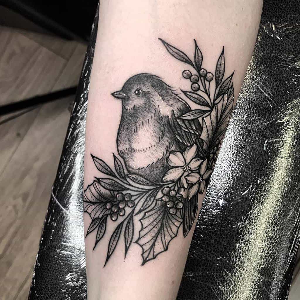 Black and white tattoo of a robin surrounded by leaves, berries, and flowers