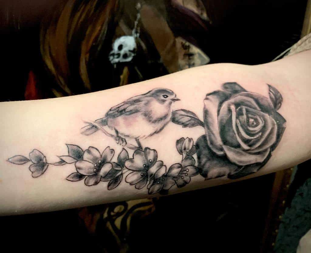 Black and grey tattoo of a robin perched on a branch with flowers and a large rose