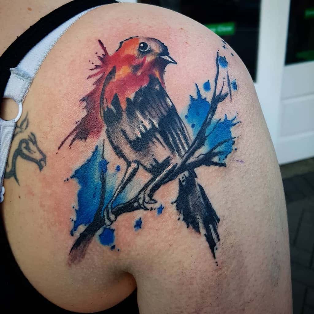 Colorful tattoo of a robin perched on a branch with blue and red splashes