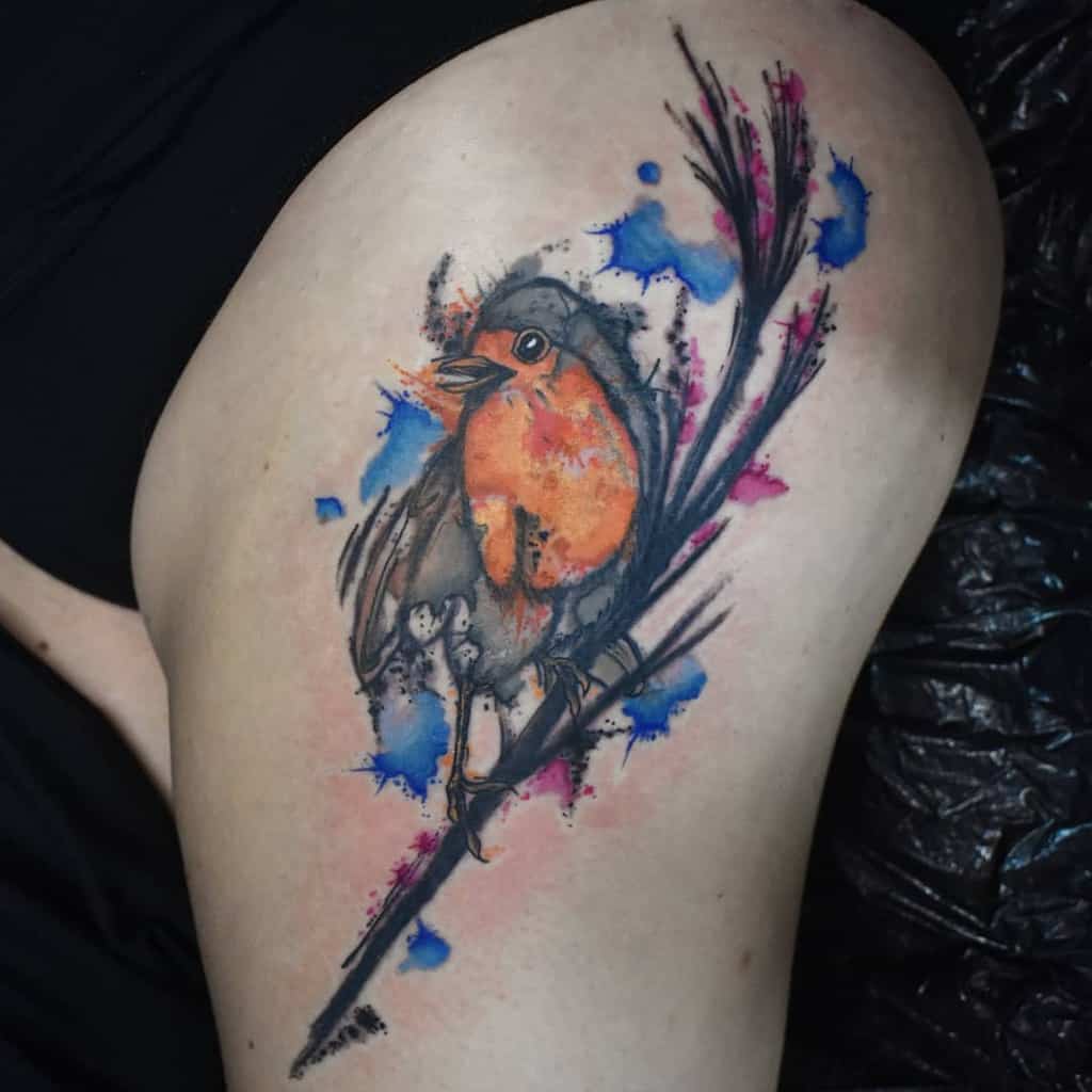 Tattoo of a robin perched on a branch with watercolor-style splashes of orange, pink and blue
