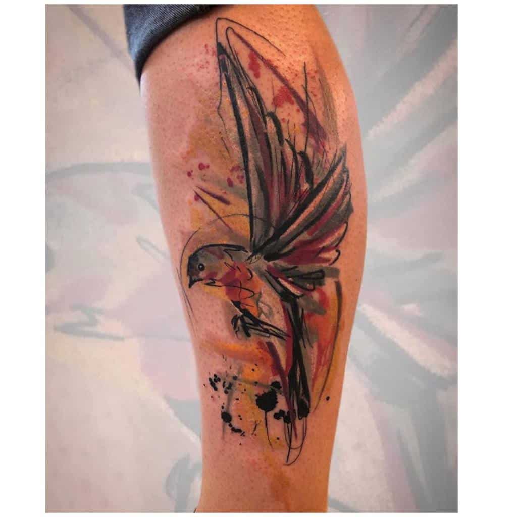 Watercolor-style tattoo of a robin with extended wings, featuring splashes of orange, black, and red