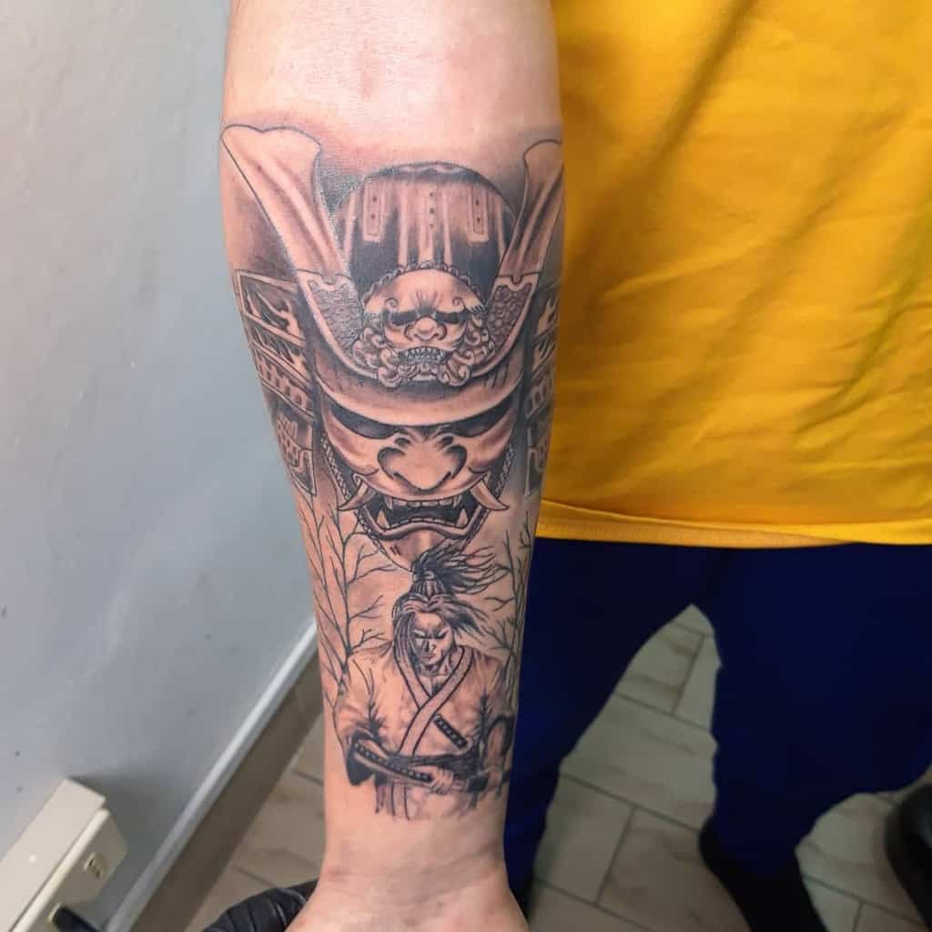 Intricate forearm tattoo featuring a fierce samurai helmet above a detailed Ronin holding a katana, framed by delicate tree branches
