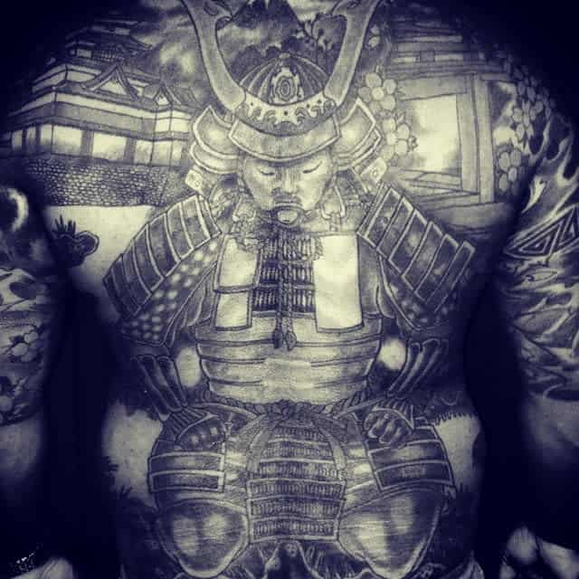 Full-back tattoo of a seated samurai in traditional armor, surrounded by Japanese architecture and detailed scenic elements