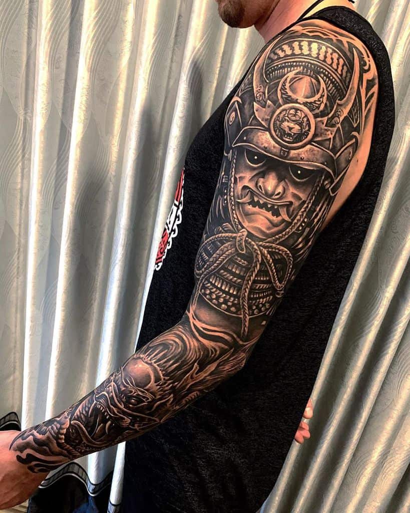 Detailed full-sleeve tattoo featuring a menacing samurai mask, intricate armor, and bold black and gray shading for a dramatic effect
