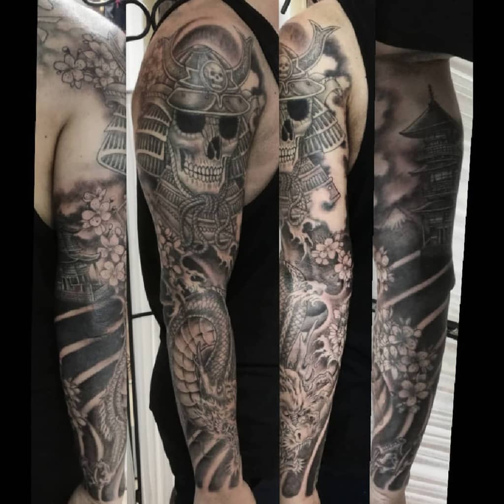 Full-sleeve tattoo featuring a skeletal samurai helmet, cherry blossoms, a coiled dragon, and a traditional Japanese pagoda in grayscale