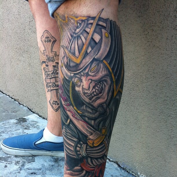 Vibrant leg tattoo depicts a fierce samurai warrior with vivid colors and bold lines, emphasizing a dynamic and intense expression of traditional Japanese art