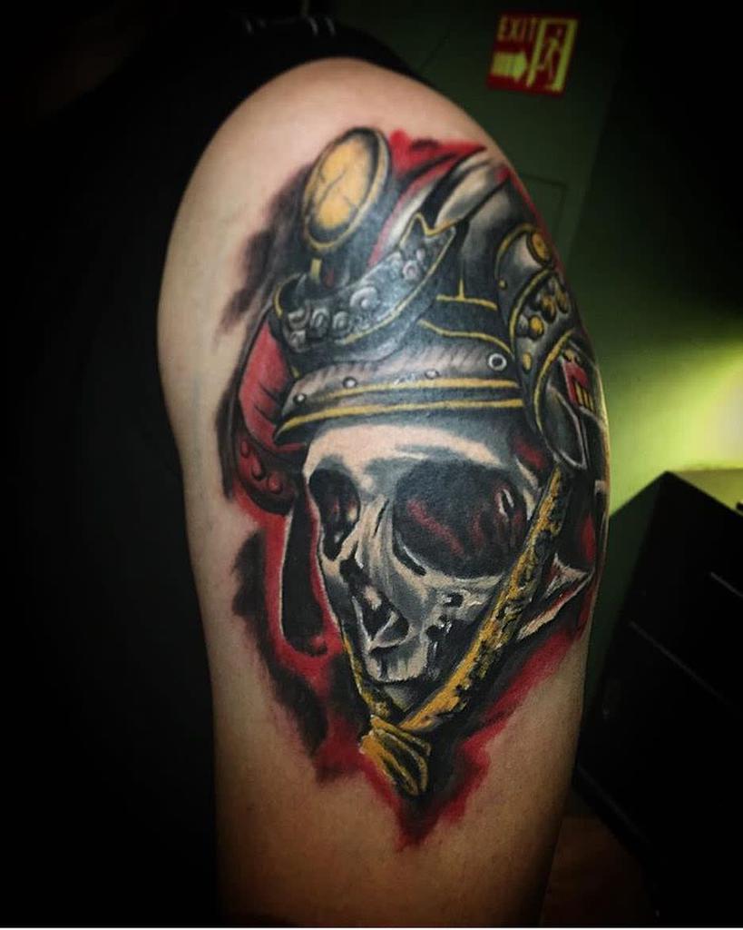 Vibrant tattoo of a samurai skull with intricate armor, highlighted with red and yellow accents, showcasing dynamic shading and bold contrasts