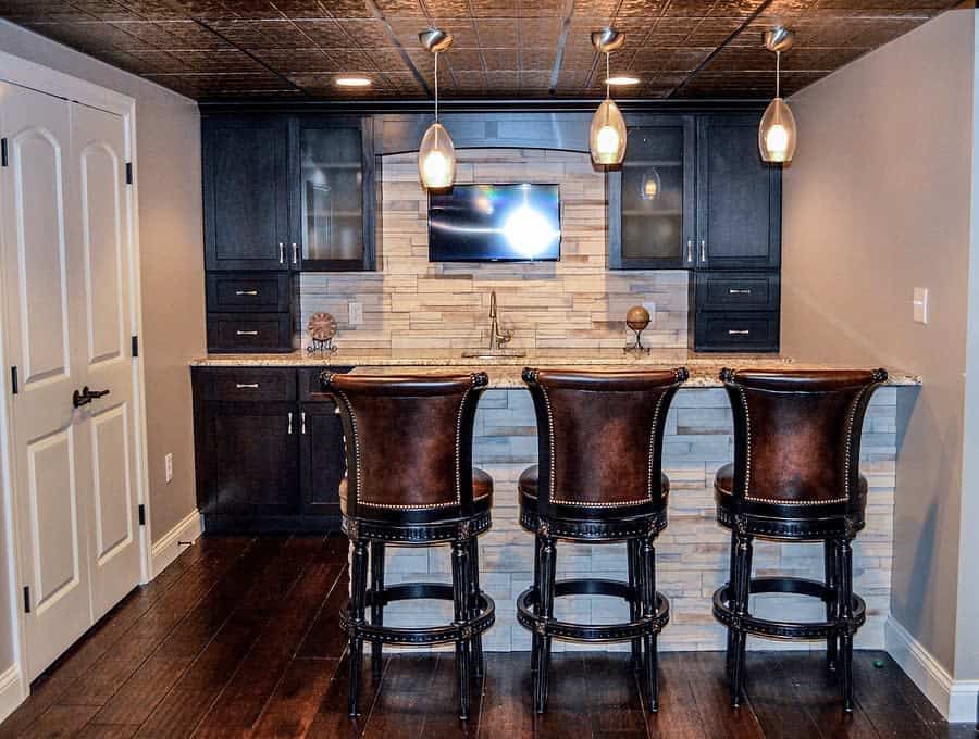 Elegant basement bar with leather bar stools, dark cabinetry, and pendant lighting.