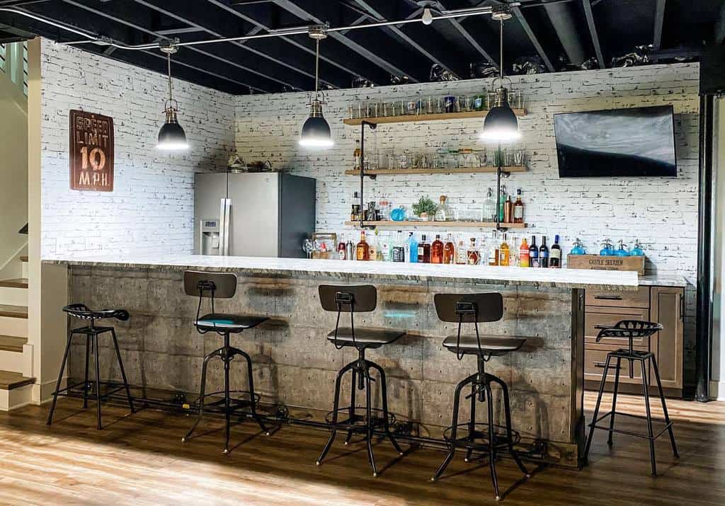 Industrial-style basement bar with metal stools, exposed ceiling, and modern pendant lighting.