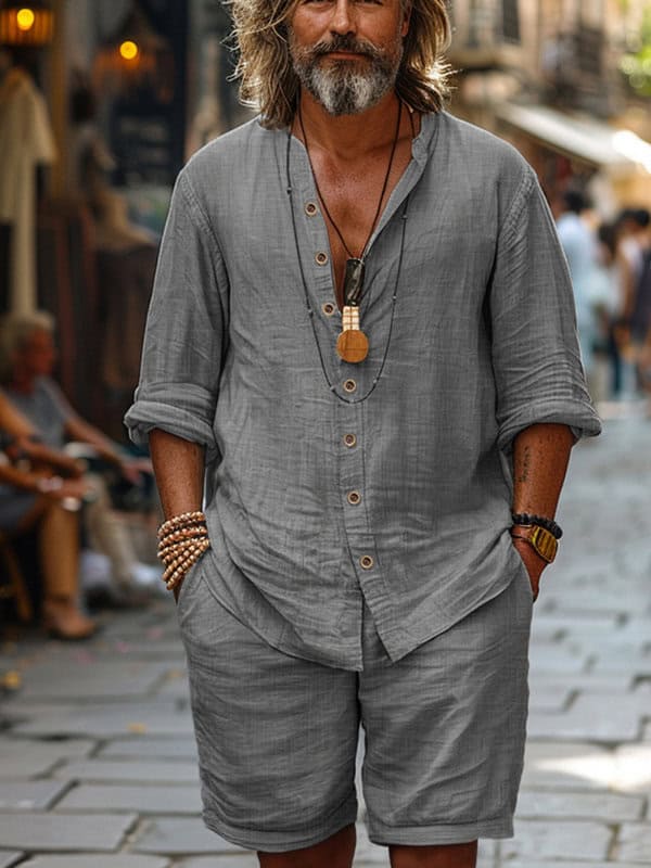 Man with long hair and beard wearing a grey buttoned shirt and matching shorts walking down a cobblestone street showcasing perfect summer outfits for men