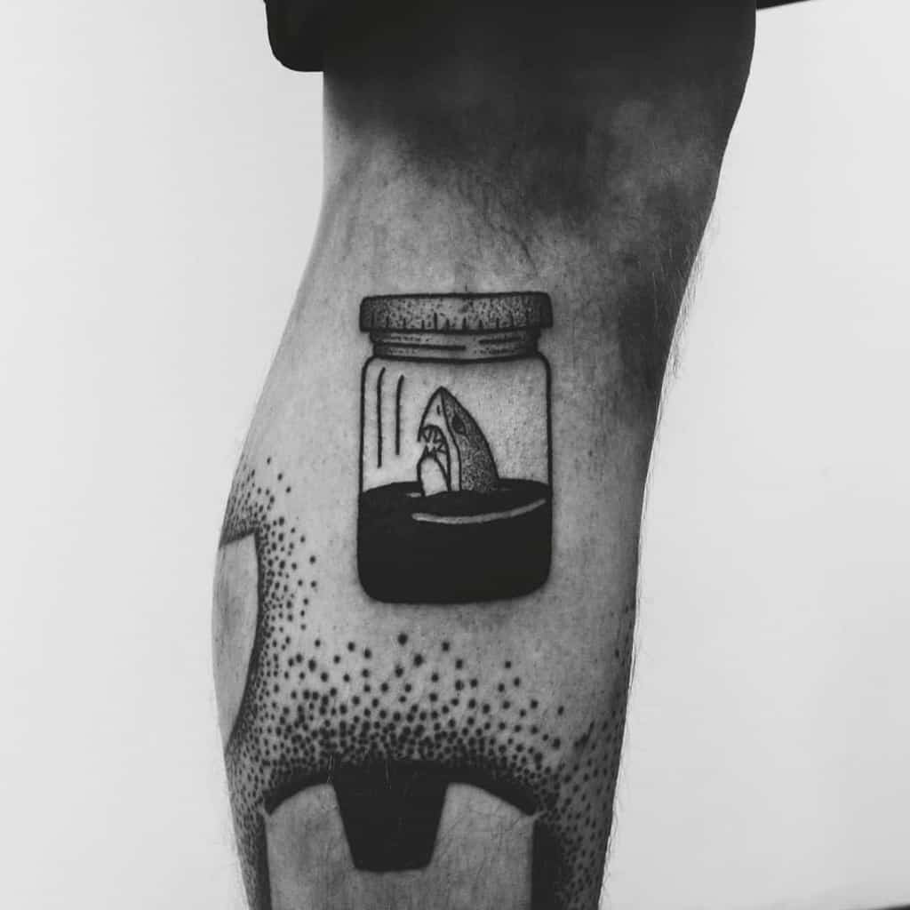 Minimalist shark tattoo featuring a shark fin emerging from dark ocean water inside a closed small jar