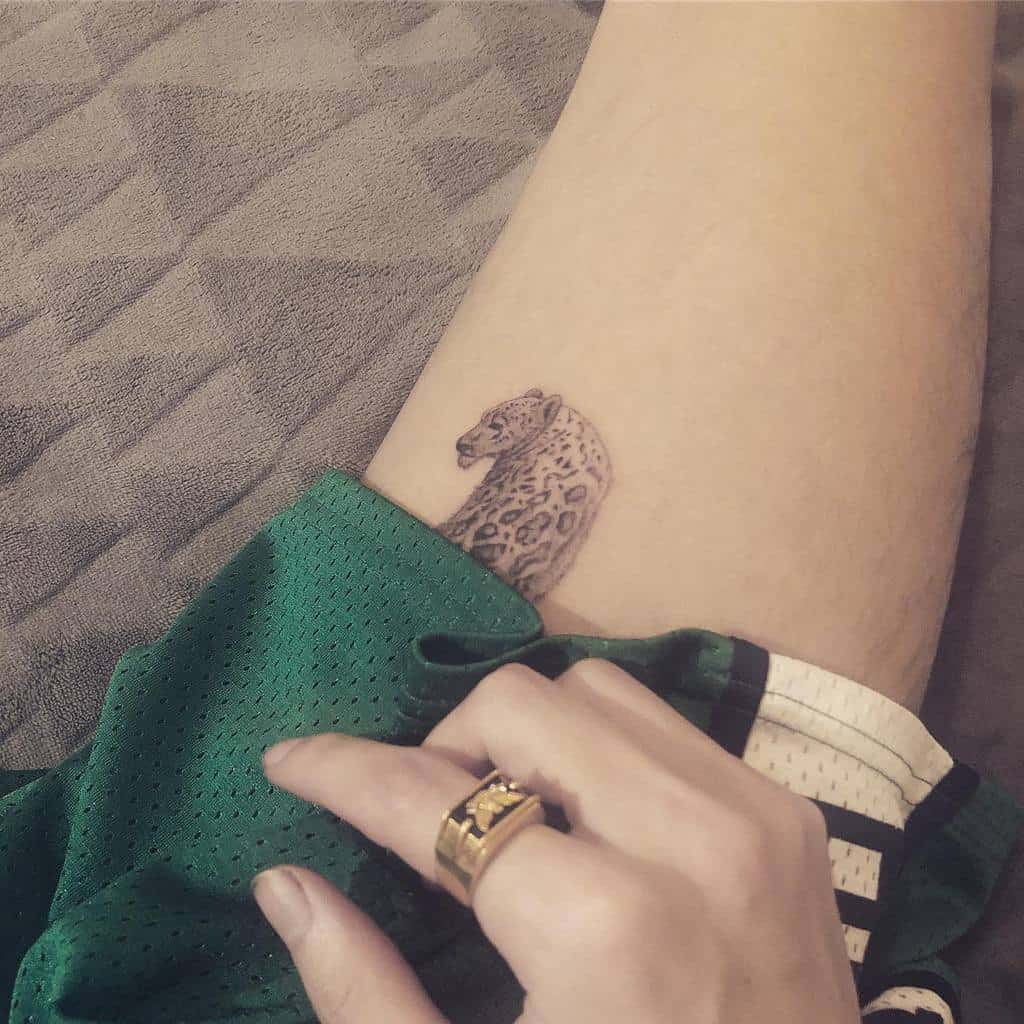 Close-up of a leopard tattoo on a thigh, created with single needle precision, with a hand resting on green shorts next to it