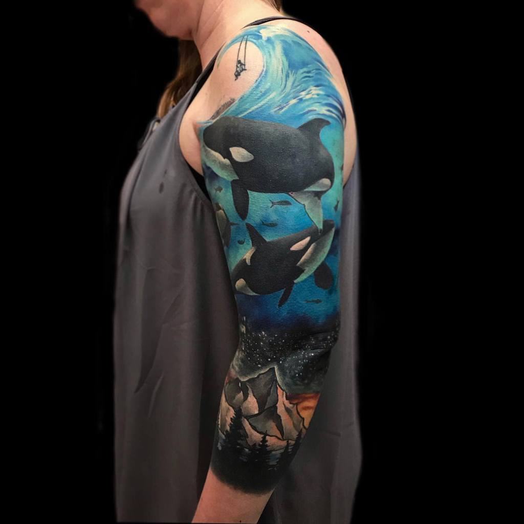 An arm with a colorful tattoo of orcas and a night scene with mountains