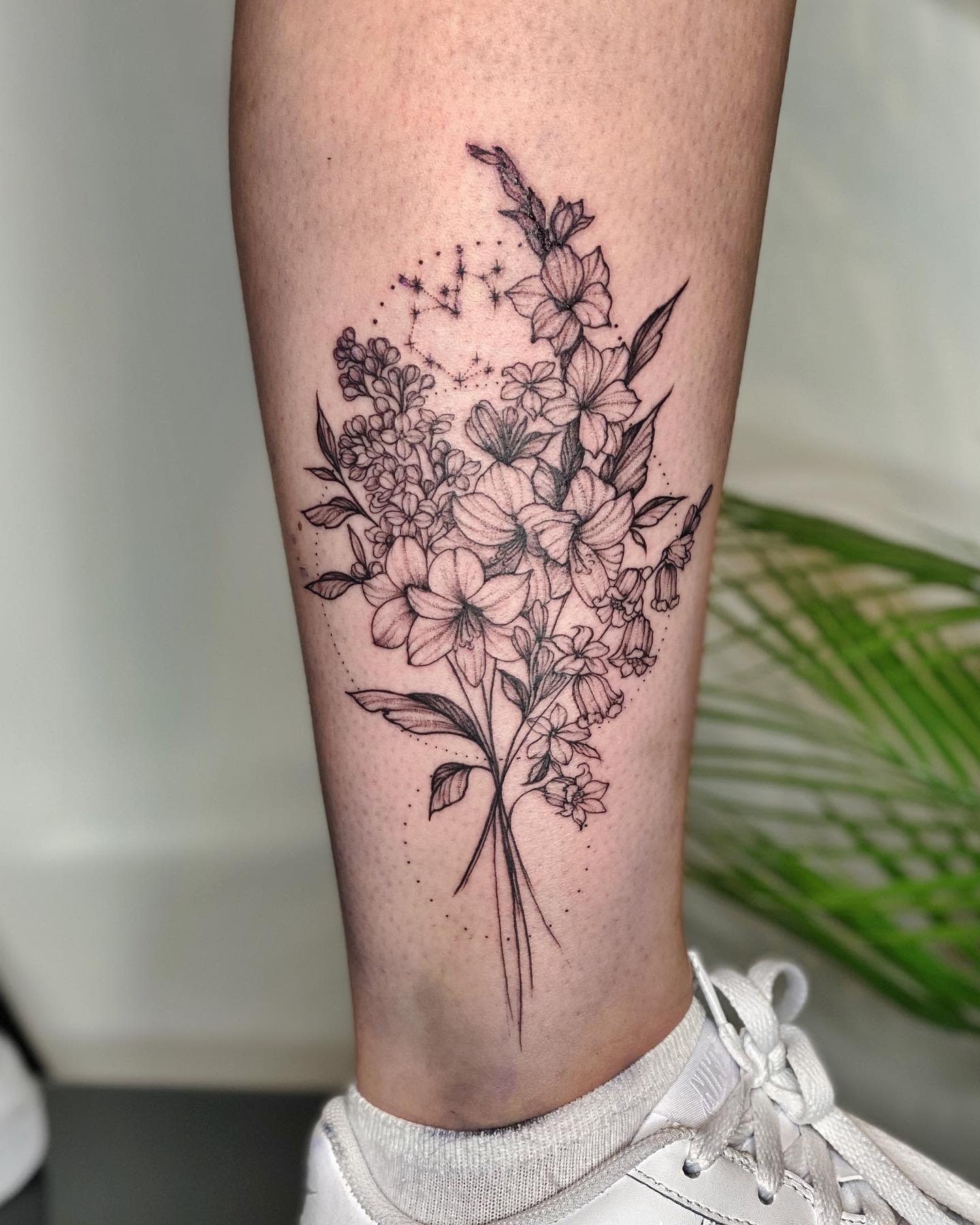 Black and grey floral tattoo on leg with delicate flowers and a small constellation