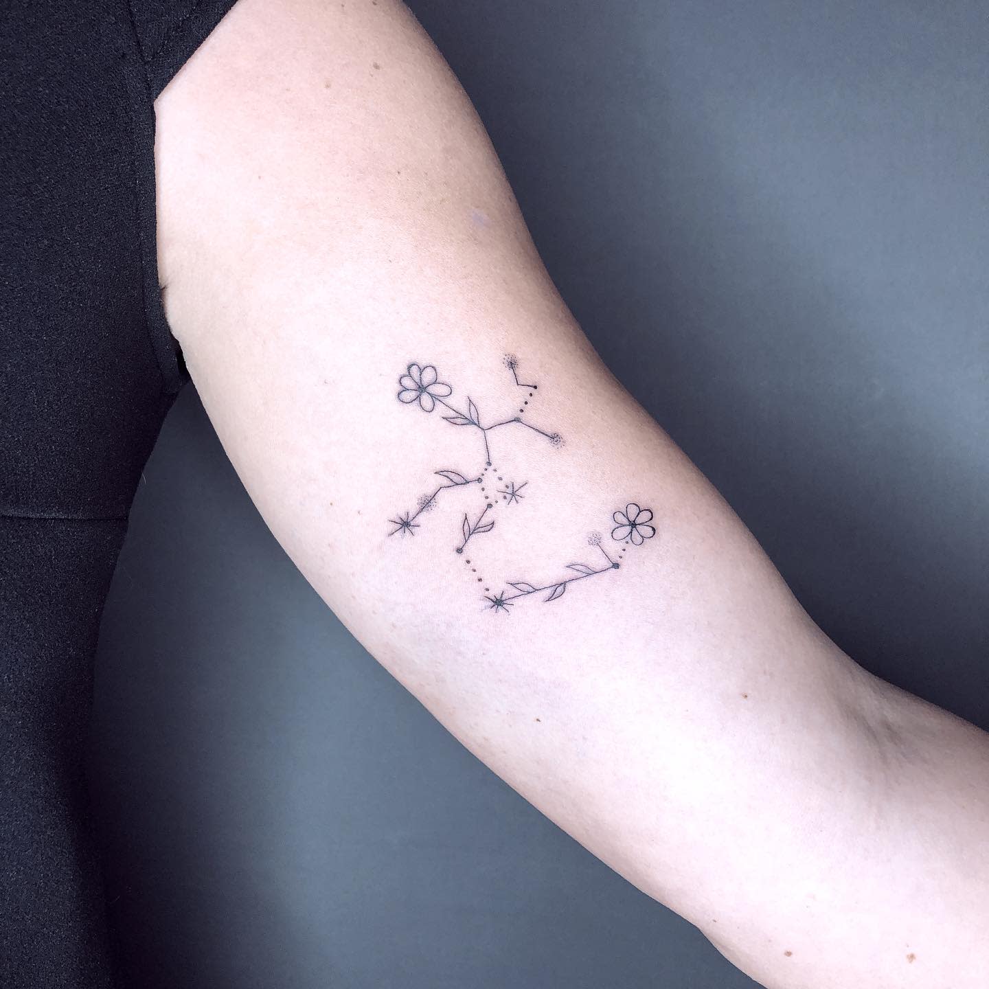 Delicate constellation tattoo with flowers on the upper arm