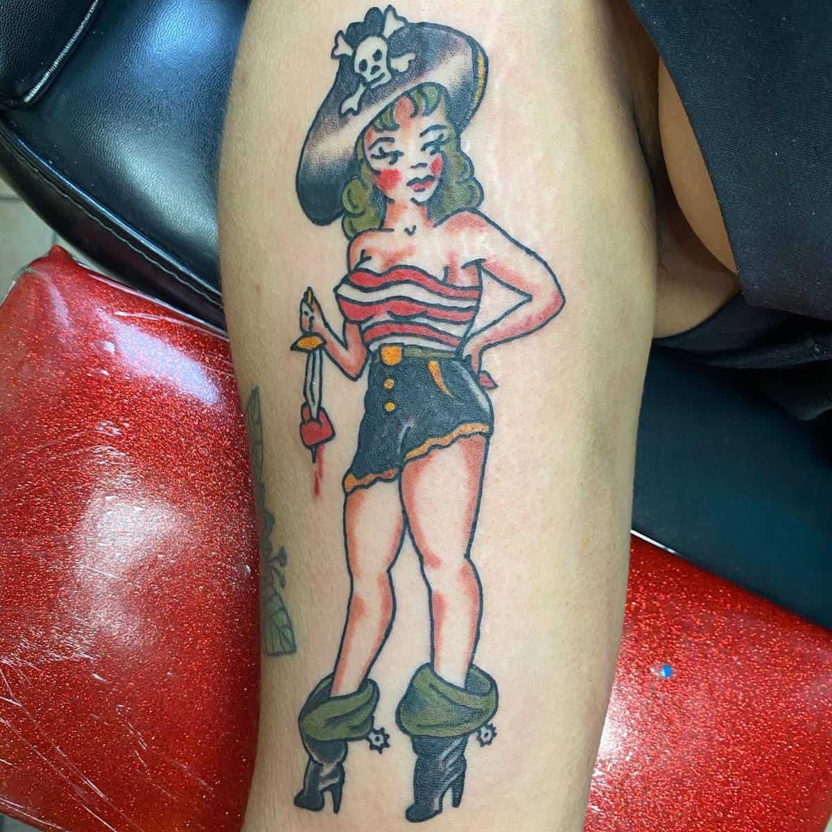 Tattoo of a female pirate with a striped top, high-waisted shorts, boots, and a hat on someone's leg
