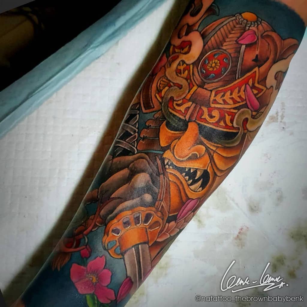 Colorful samurai tattoo with a fierce orange mask, intricate armor details, pink floral accents, and dynamic smoke elements