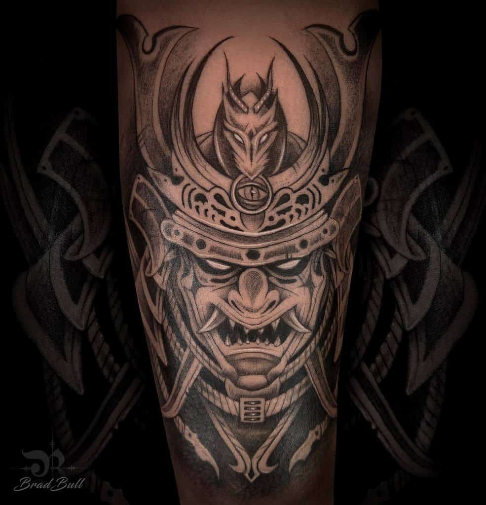 Black-and-gray samurai tattoo with a menacing mask, ornate helmet, and wolf emblem, showcasing detailed shading and bold design