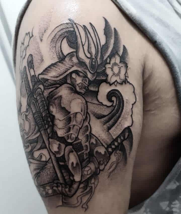 Bold black-and-gray samurai tattoo featuring a dynamic pose, detailed armor, katana, swirling smoke, and floral accents