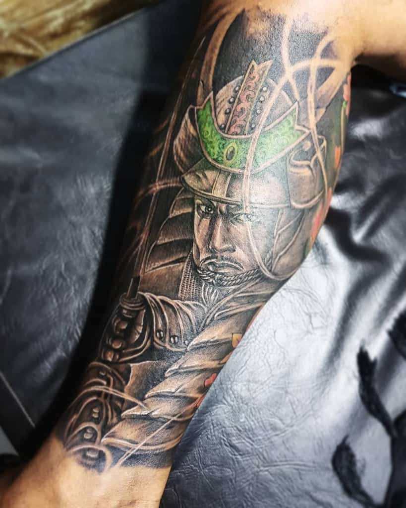 Vivid samurai tattoo featuring a detailed warrior's face with a green helmet, katana, and intricate shading, complemented by vibrant accent colors