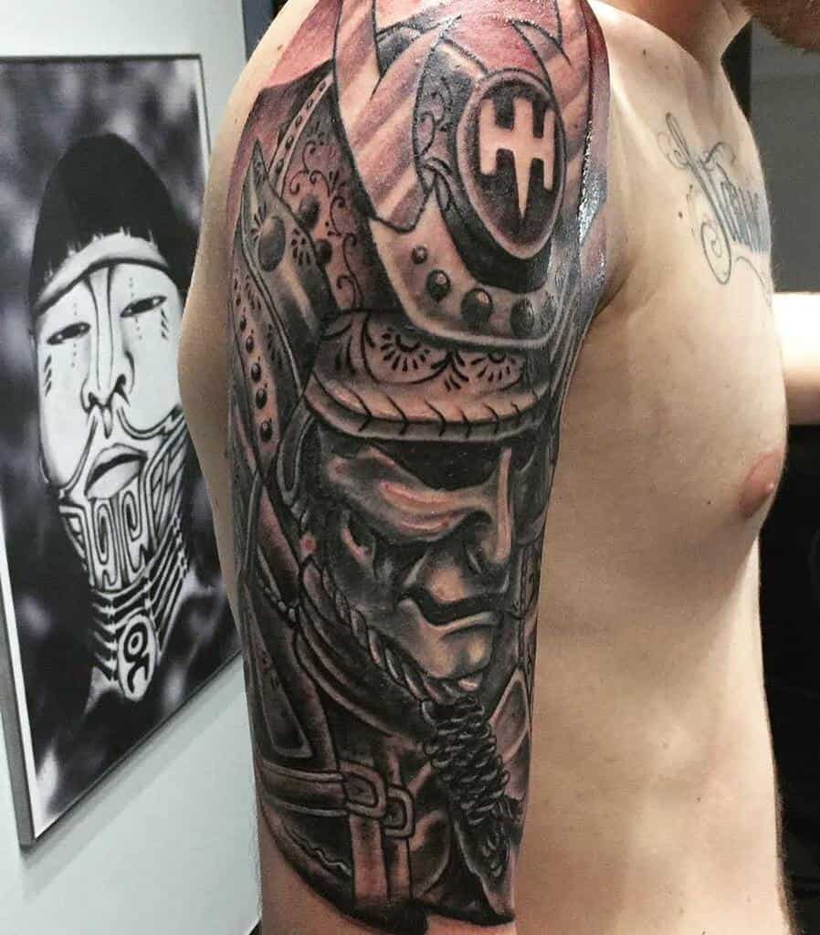 Detailed black-and-gray samurai tattoo with intricate armor details, fierce facial expression, and dramatic shading on the arm