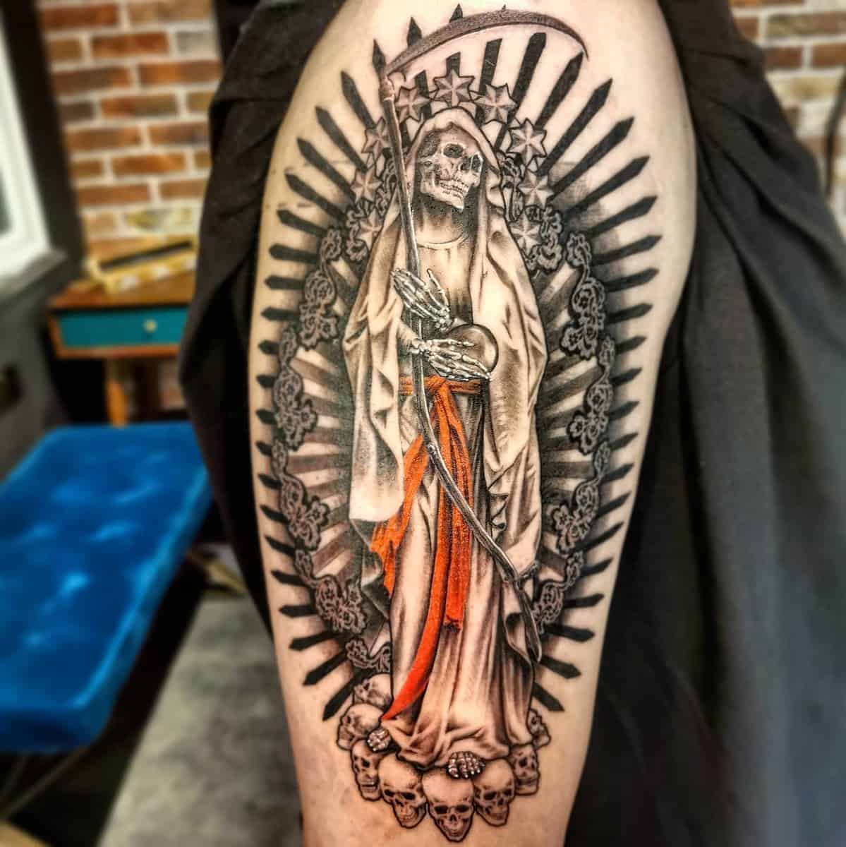 Santa Muerte tattoo with scythe, radiant lines, skulls, and orange accents on her cloak