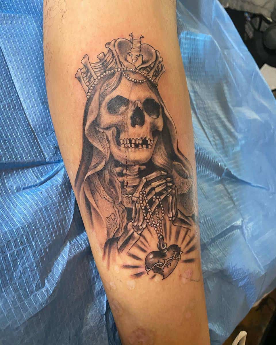 Santa Muerte tattoo with crowned skeleton holding a rosary and heart, symbolizing faith and mortality