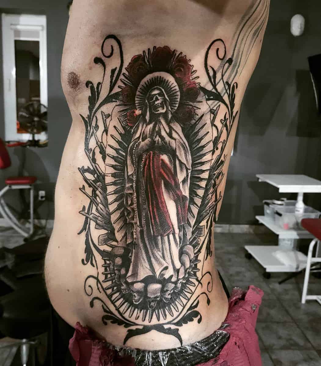 Santa Muerte tattoo on the ribs, depicting the skeletal saint with intricate shading, red accents, and ornate details