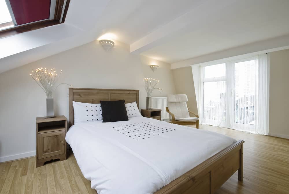 Minimalist attic bedroom with wood floors, balcony, and simple wooden bed.