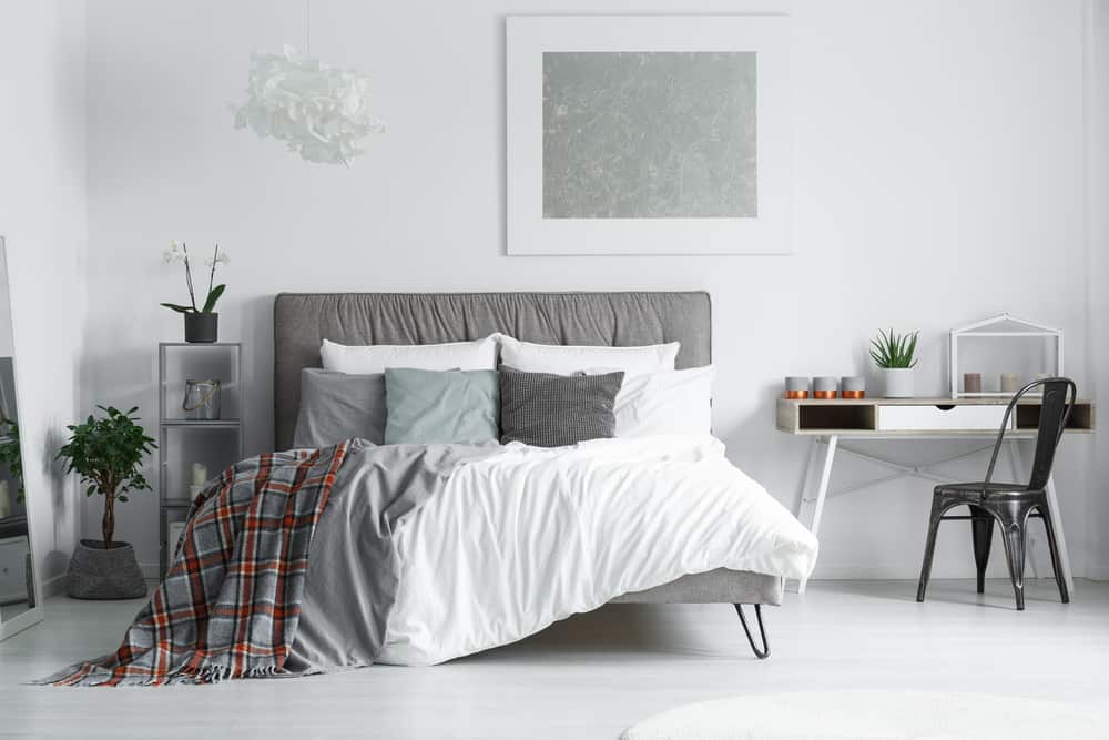 Modern white bedroom with gray headboard small desk and potted plants.
