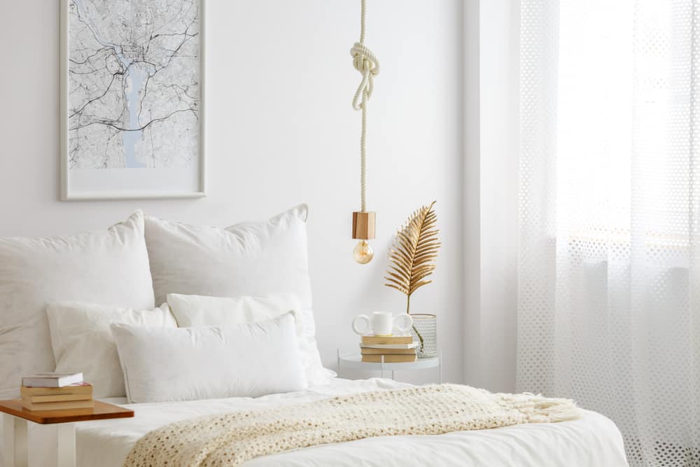 Minimalist bedroom with rope pendant light, cozy bedding, and wall art.