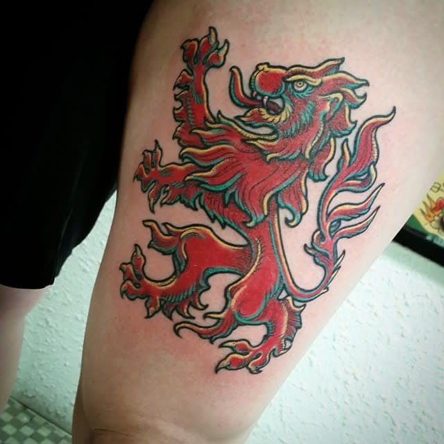 Tattoo of a red and green Scottish lion with a touch of yellow, has open mouth with long tongue and raised paw