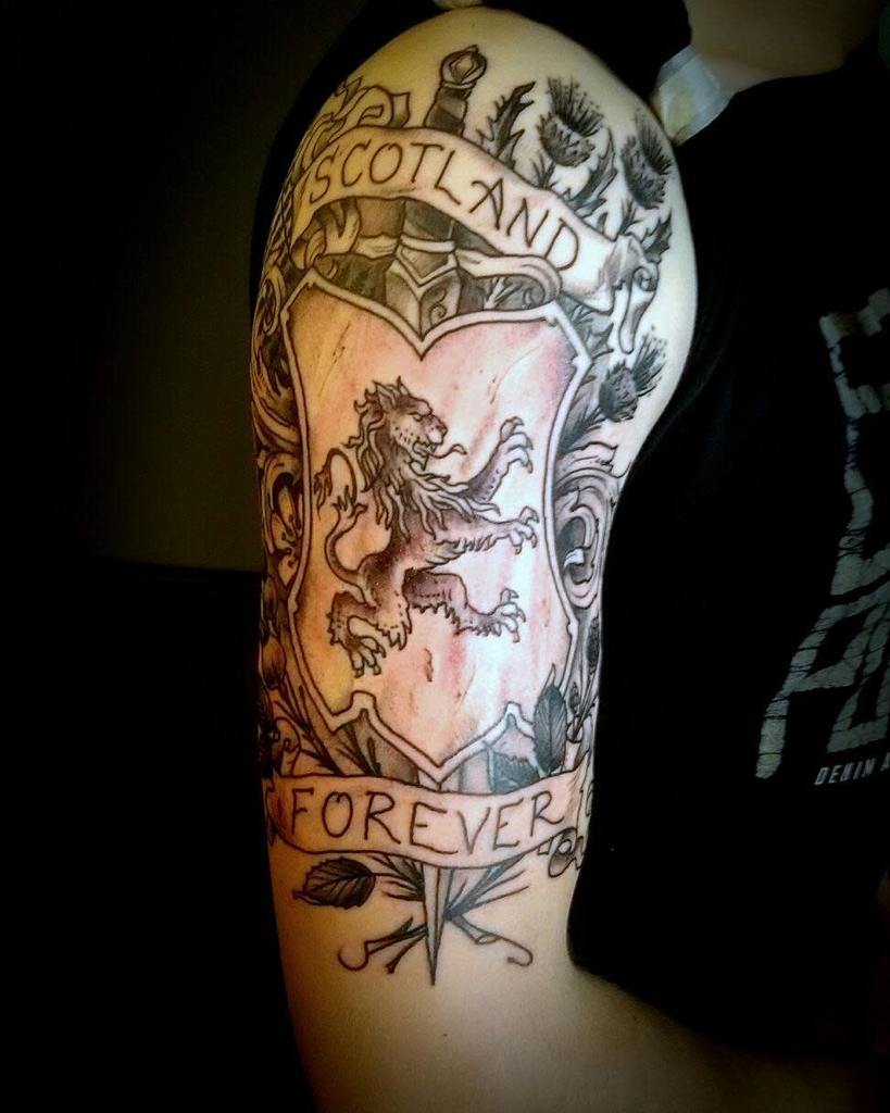 Arm tattoo with a Scottish lion crest and text reading "Scotland Forever," featuring thistle, leaves and sword motifs