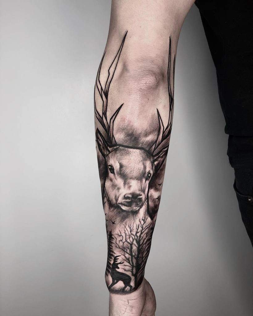 A majestic Scottish stag tattoo with intricate antlers, set against a misty forest backdrop, featuring a silhouetted deer beneath a bare tree