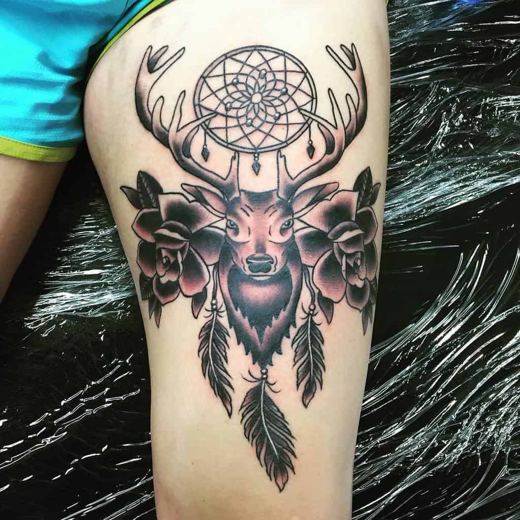 Black and grey tattoo of a Scottish stag, above the antler is a dreamcatcher and below it is a flowers, and hanging feather