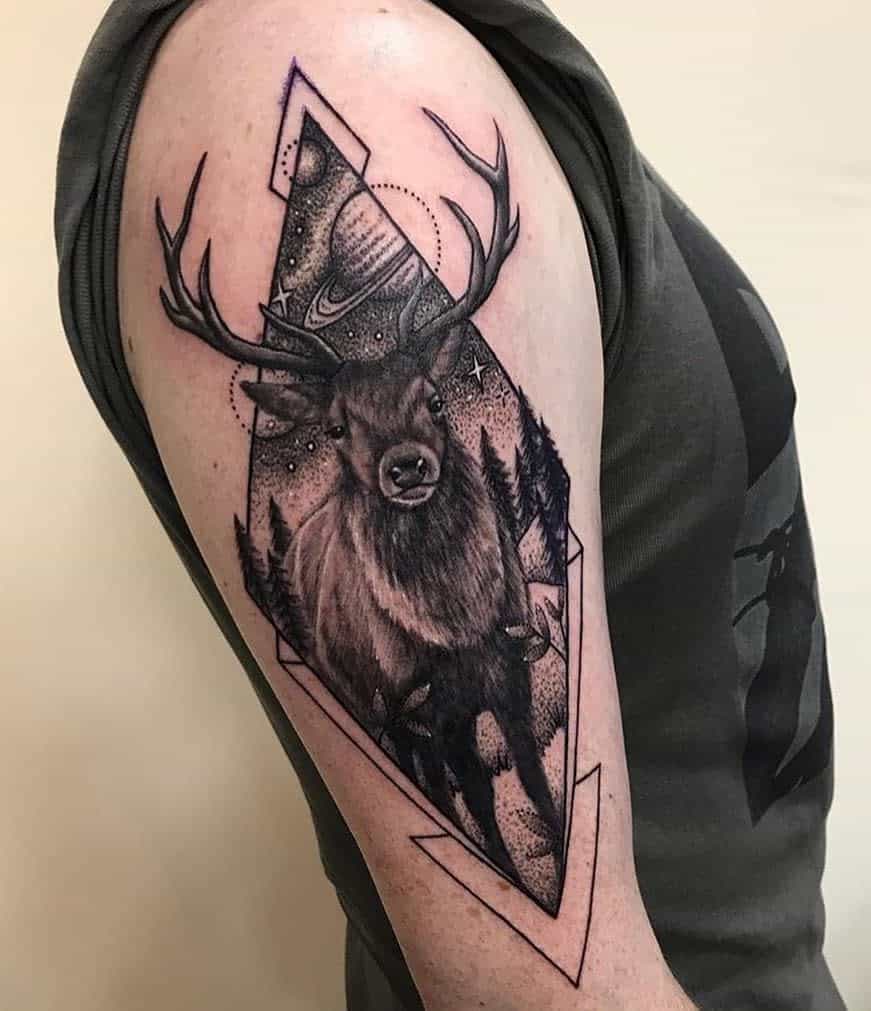 Tattoo of a Scottish stag with antlers on an arm, framed by geometric shapes and forest scenery with stars and Saturn