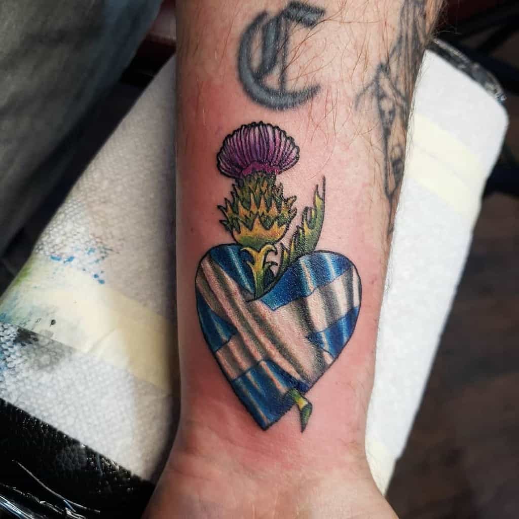 Colorful tattoo of a Scottish thistle emerging from a heart-shaped tartan pattern