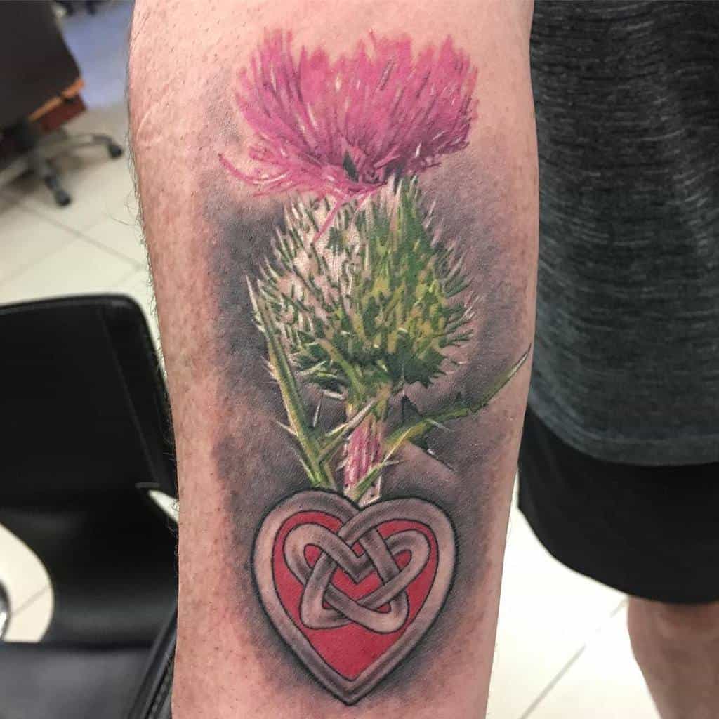 Colorful tattoo of a pink Scottish thistle above a heart symbol with a knot design