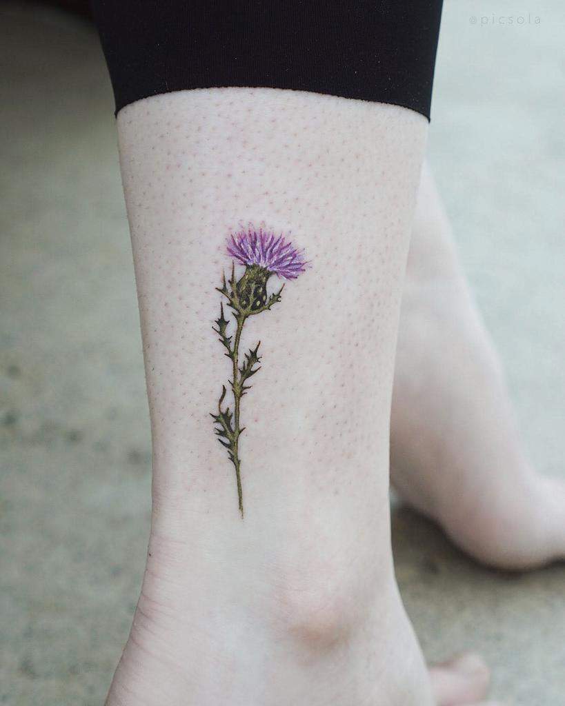Simple and elegant tattoo of a single Scottish thistle with a purple flower
